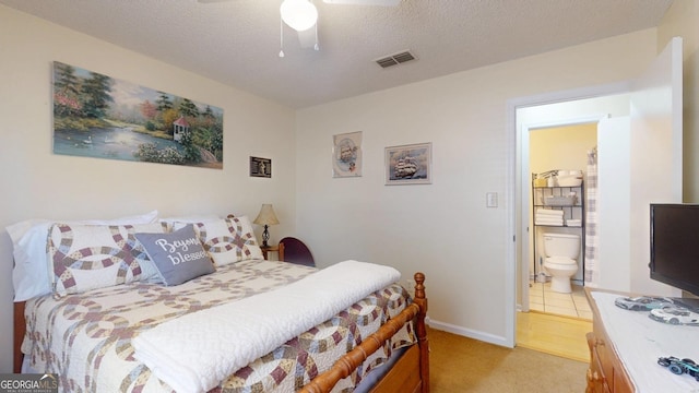 bedroom with visible vents, ceiling fan, light colored carpet, ensuite bathroom, and a textured ceiling