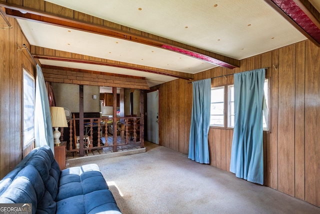 unfurnished living room featuring beamed ceiling, wood walls, and carpet flooring