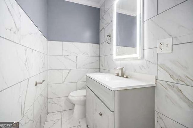 half bathroom featuring toilet, tile walls, ornamental molding, and vanity