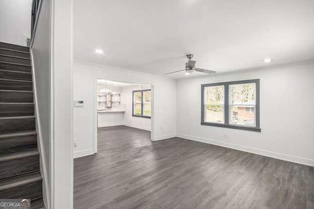 unfurnished living room with stairway, baseboards, dark wood-style flooring, and ceiling fan with notable chandelier