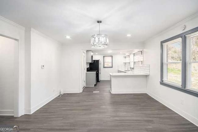 kitchen with dark wood finished floors, a peninsula, freestanding refrigerator, crown molding, and a notable chandelier