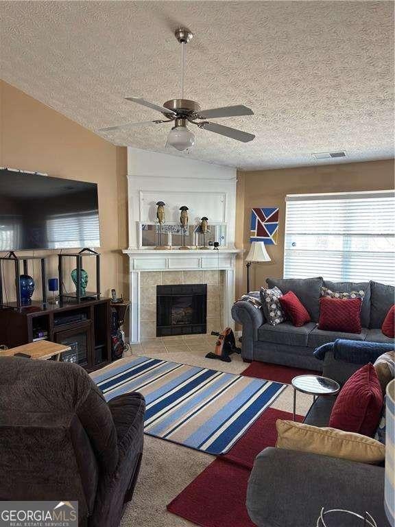 living area with visible vents, carpet, vaulted ceiling, a tile fireplace, and a ceiling fan