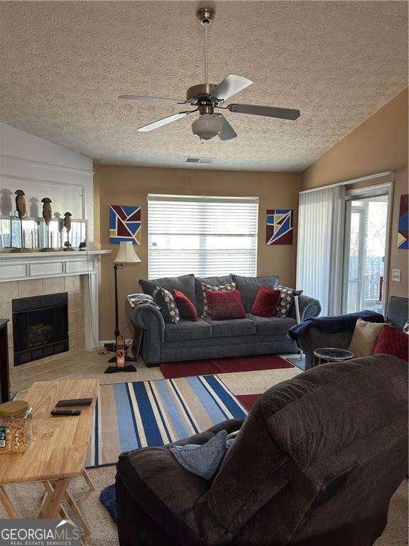 living room featuring a tile fireplace, a healthy amount of sunlight, visible vents, and ceiling fan