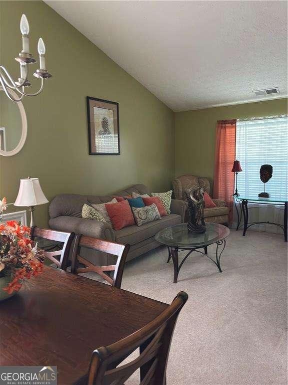 living area featuring visible vents, light colored carpet, and vaulted ceiling