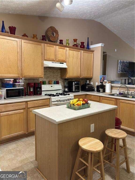 kitchen with black microwave, under cabinet range hood, a kitchen bar, white range with gas stovetop, and a sink