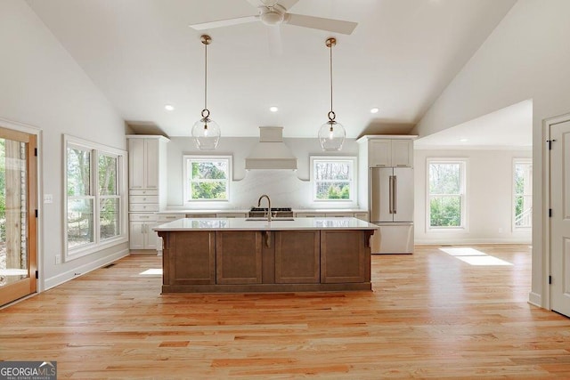 kitchen featuring light wood finished floors, high end fridge, light countertops, and custom range hood