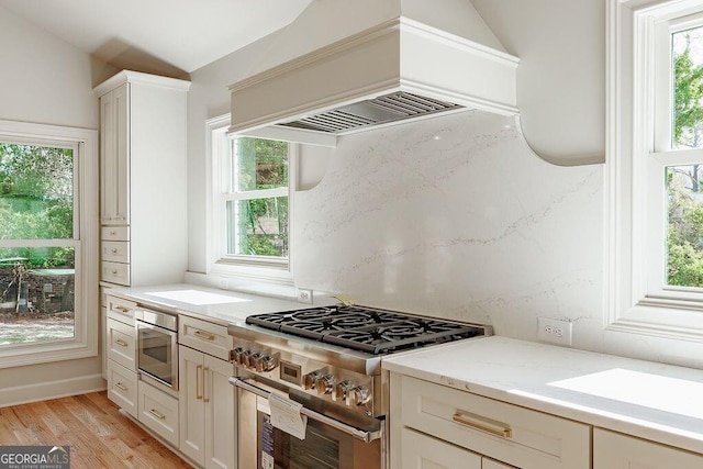 kitchen featuring light stone countertops, custom range hood, decorative backsplash, light wood-style floors, and stainless steel stove