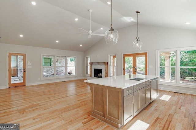 kitchen with an island with sink, a sink, light countertops, dishwasher, and light wood-type flooring