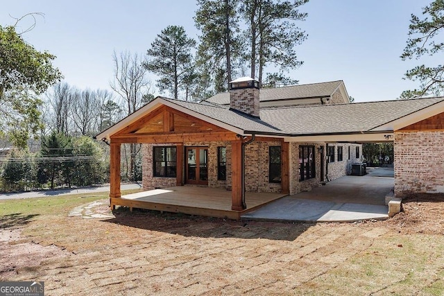 back of house featuring a shingled roof, central AC unit, french doors, a chimney, and a deck