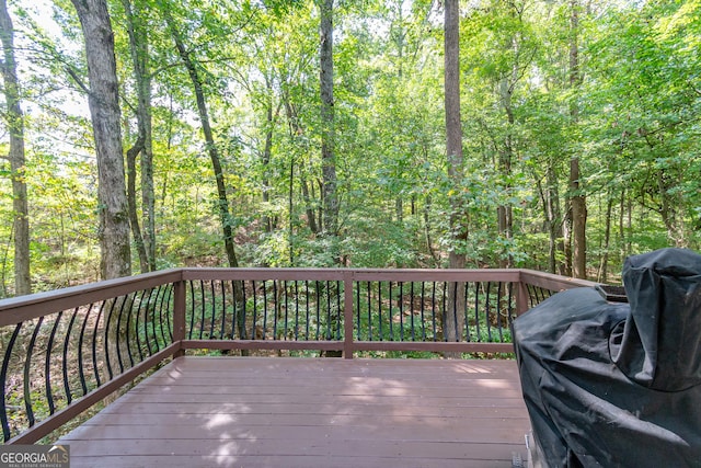 wooden deck featuring a forest view and a grill