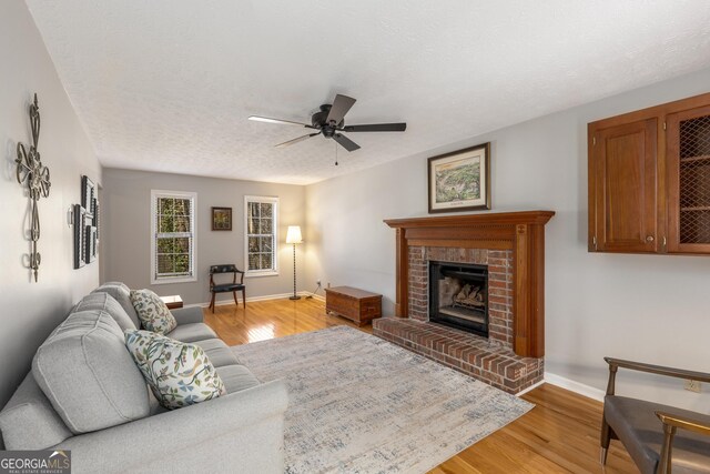 living room featuring a ceiling fan, baseboards, light wood finished floors, a fireplace, and a textured ceiling