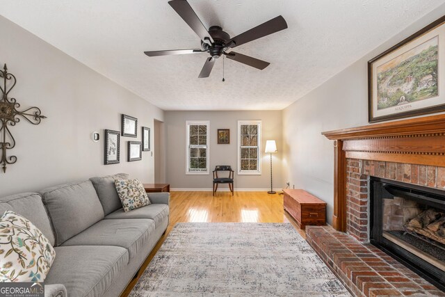 living room with a ceiling fan, a textured ceiling, wood finished floors, a fireplace, and baseboards