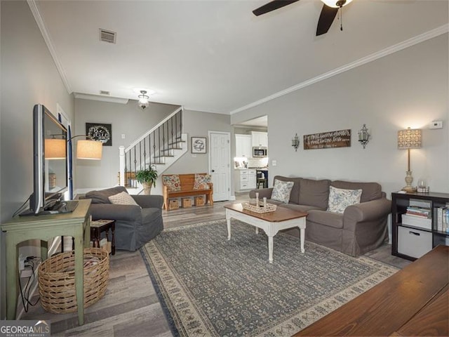 living room with visible vents, a ceiling fan, wood finished floors, crown molding, and stairs