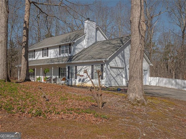 view of front of house with fence, driveway, covered porch, a chimney, and a garage