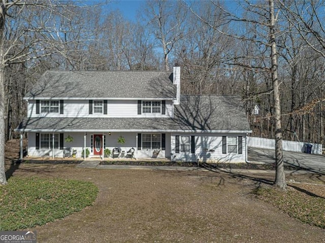 view of front facade featuring fence, covered porch, roof with shingles, and a chimney