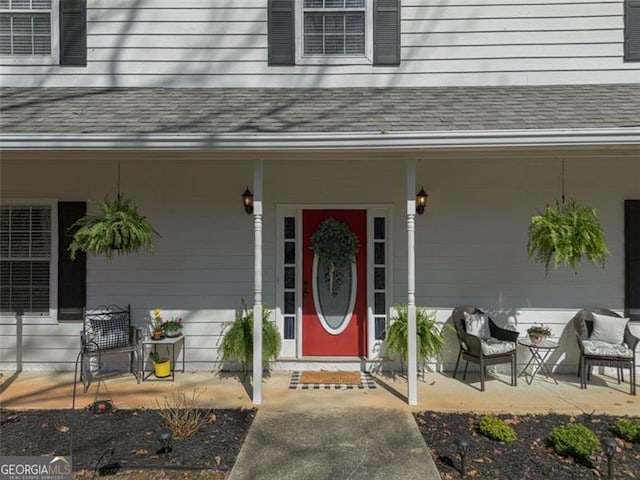 doorway to property featuring a patio area, covered porch, and roof with shingles