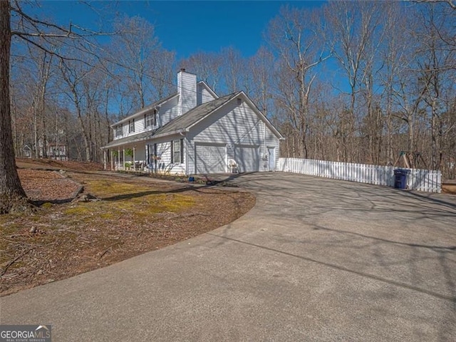 view of property exterior with a garage, concrete driveway, a chimney, and fence