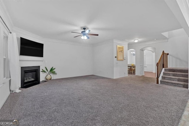 unfurnished living room featuring carpet, arched walkways, ceiling fan, stairs, and crown molding