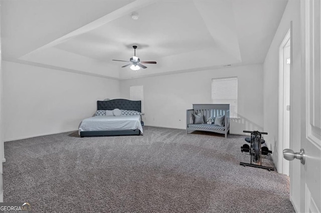 carpeted bedroom with ceiling fan, baseboards, and a tray ceiling