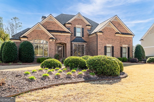 traditional-style home featuring a shingled roof, brick siding, and a chimney