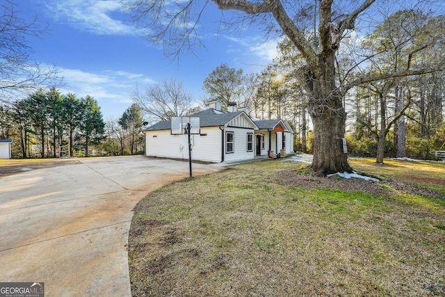 view of front facade with driveway, a chimney, a front yard, and roof with shingles