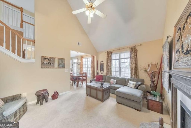 carpeted living room with visible vents, baseboards, ceiling fan with notable chandelier, a fireplace, and high vaulted ceiling