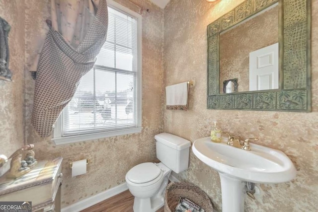 bathroom with baseboards, toilet, wood finished floors, and wallpapered walls