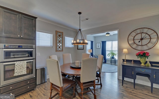 dining space with wood finished floors, visible vents, baseboards, crown molding, and ceiling fan with notable chandelier