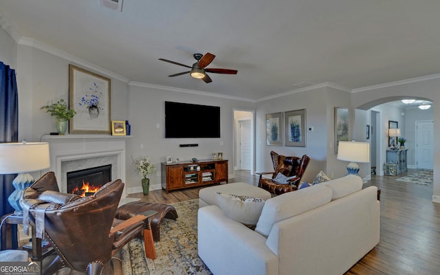 living room with wood finished floors, arched walkways, crown molding, a premium fireplace, and ceiling fan