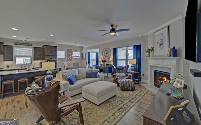 living room featuring ornamental molding, a ceiling fan, wood finished floors, recessed lighting, and a fireplace