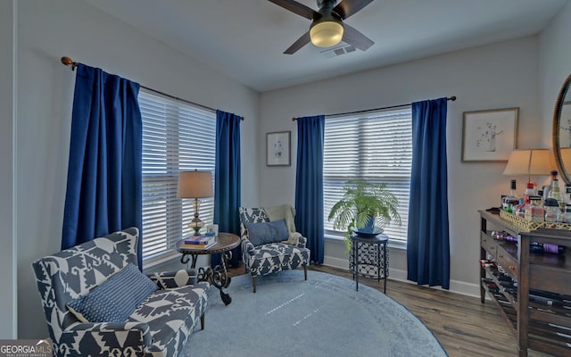 sitting room with wood finished floors, a ceiling fan, visible vents, and baseboards