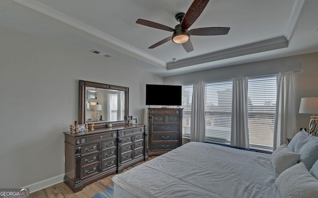 bedroom with visible vents, ornamental molding, wood finished floors, baseboards, and a raised ceiling