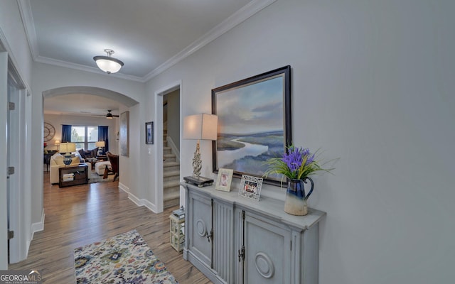 hallway with stairway, arched walkways, wood finished floors, and ornamental molding