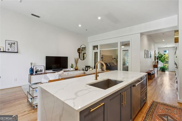 kitchen featuring light stone counters, open floor plan, light wood-style flooring, and a sink