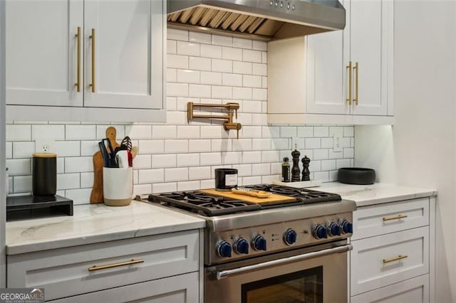 kitchen with light stone countertops, stainless steel range, white cabinetry, exhaust hood, and tasteful backsplash