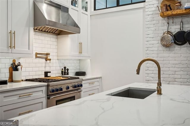 kitchen featuring a sink, white cabinetry, decorative backsplash, extractor fan, and high end range