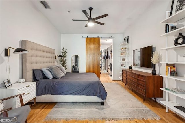 bedroom featuring wood finished floors, visible vents, ceiling fan, a spacious closet, and a barn door