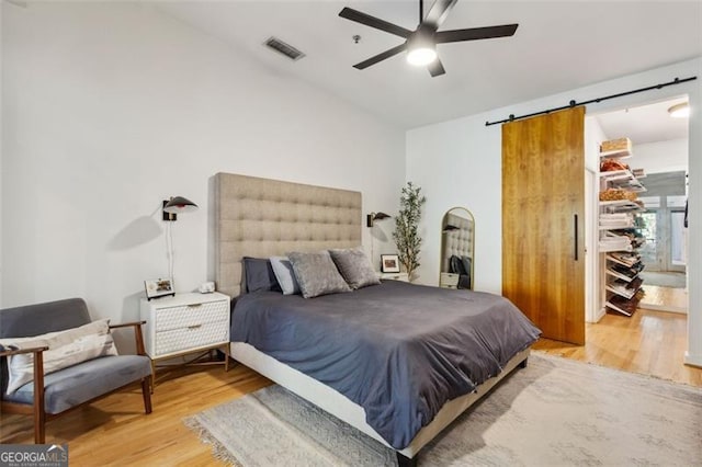 bedroom featuring ceiling fan, a barn door, visible vents, and light wood-type flooring