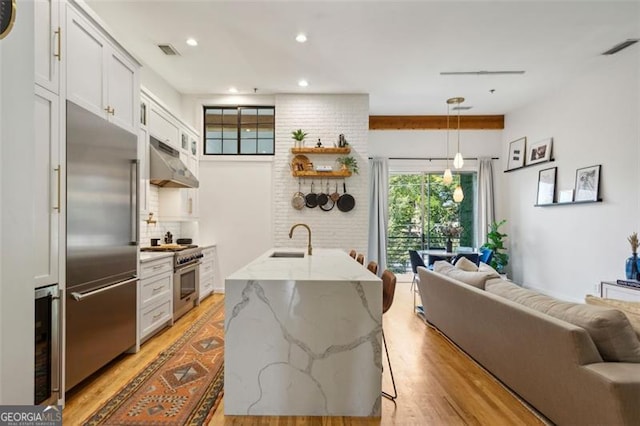 kitchen featuring a sink, open floor plan, under cabinet range hood, high quality appliances, and light wood-type flooring