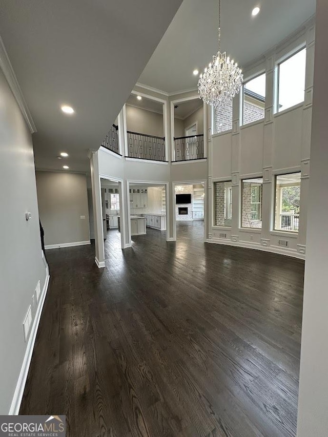 unfurnished living room with dark wood-style floors, baseboards, ornamental molding, a towering ceiling, and a notable chandelier