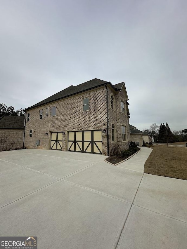 view of side of property featuring a garage, brick siding, and concrete driveway