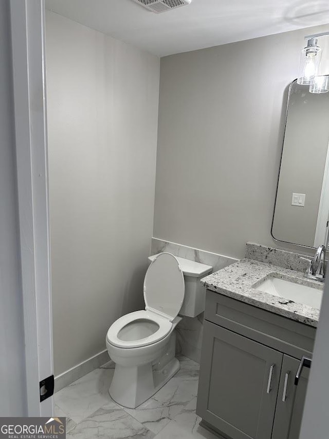 bathroom with vanity, toilet, baseboards, and marble finish floor