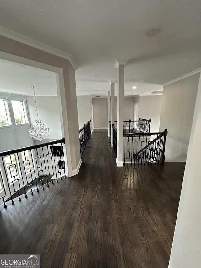 corridor featuring dark wood-type flooring, baseboards, ornamental molding, an upstairs landing, and an inviting chandelier