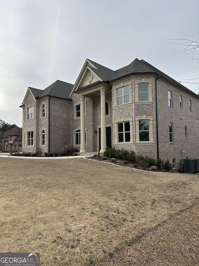 view of front facade featuring brick siding, central AC unit, and a front yard