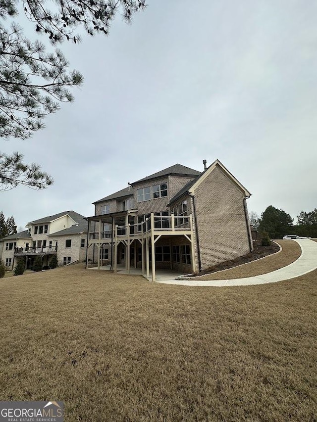 back of house with a wooden deck, a lawn, and brick siding