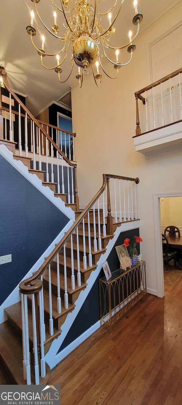 stairs with an inviting chandelier, crown molding, wood finished floors, and baseboards