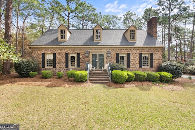 cape cod-style house featuring brick siding, a chimney, a front lawn, and roof with shingles