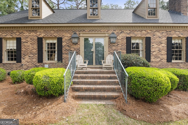 view of exterior entry featuring brick siding, a chimney, and a shingled roof