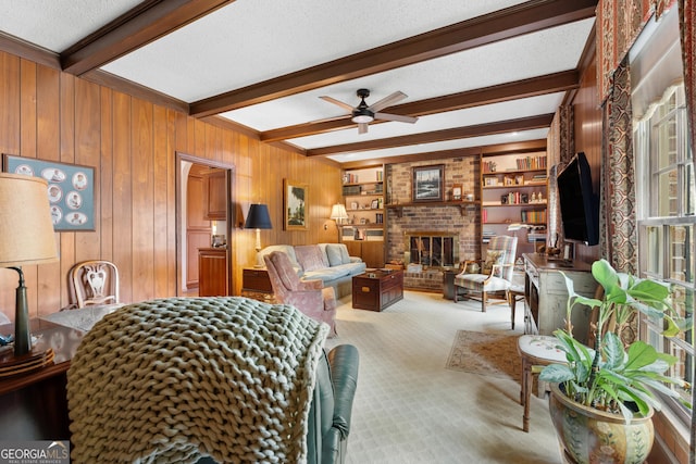 carpeted living area featuring a ceiling fan, beam ceiling, wood walls, a textured ceiling, and a brick fireplace