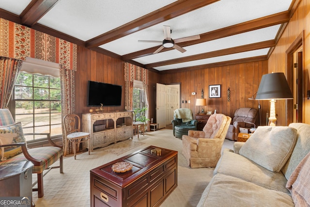 living area featuring beam ceiling, wood walls, light colored carpet, and a ceiling fan